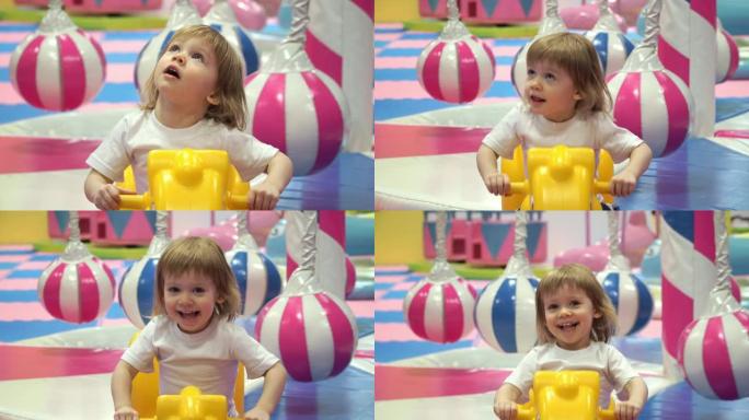小漂亮的蹒跚学步的女孩骑着玩具黄马，在儿童游戏中心微笑