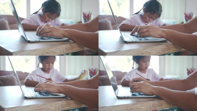 当女孩做作业时，关闭母亲在电脑笔记本电脑键盘上打字。由于Covid 19大流行，孩子在家上学，父母在