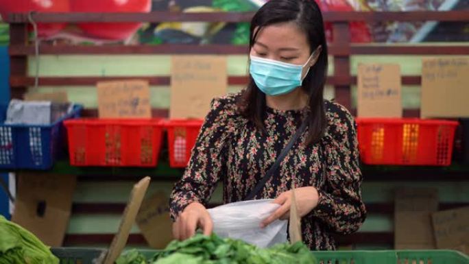 年轻的亚洲妇女戴着保护面罩在超市买新鲜蔬菜