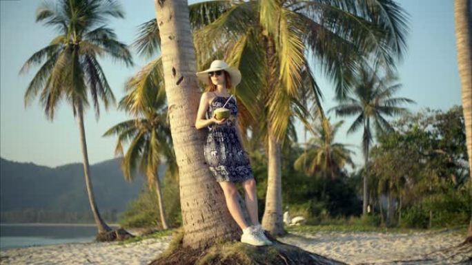 年轻女子喜欢在热带岛屿上喝椰子鸡尾酒。静态图片与移动的衣服。循环。电影胶片