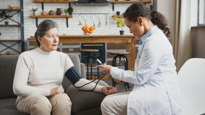 女医生在家中接受医疗咨询时，用血压袖带测量老年女性的血压，坐在沙发上