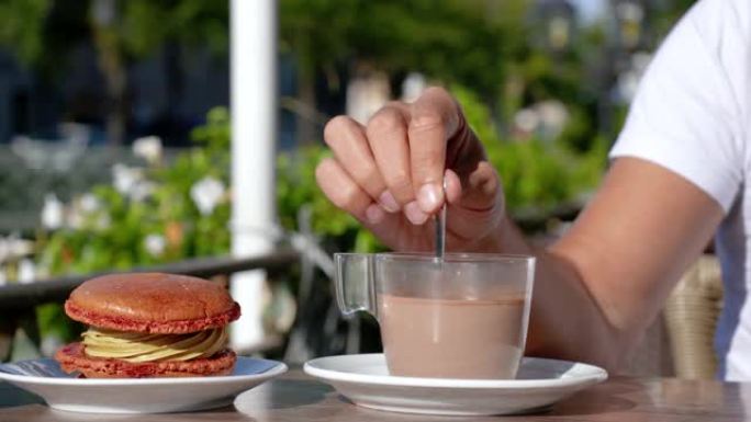 一杯热巧克力和一个橙色蛋糕。这个女人正在法国的一个露台上用勺子搅拌热巧克力。