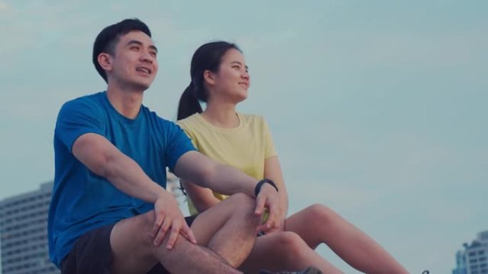 跑步和坐在海边看着美丽的日落后休息的夫妇的微笑。健康生活方式的概念，运动的人在户外训练。
