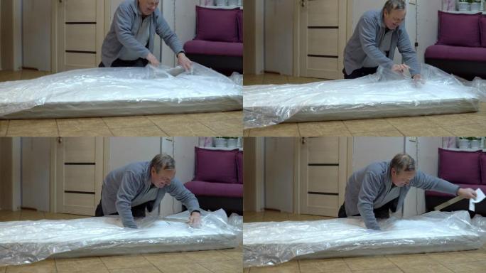 一个成年人打开一个新床垫。用压入袋子的刀打开床垫的包装
