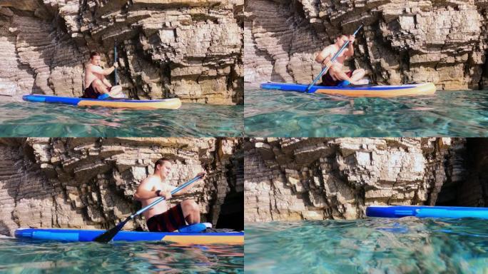 穿着防护礁石鞋的运动青年正划水，向前游泳，坐在莲花位置的SUP板上，侧视图。相机位于水面
