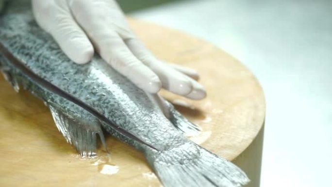 准备食物，厨师的手在厨房的木板上切片和切割新鲜的鲈鱼。