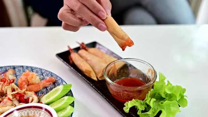 女人吃春卷配虾和甜辣椒酱。亚洲开胃菜和食物。