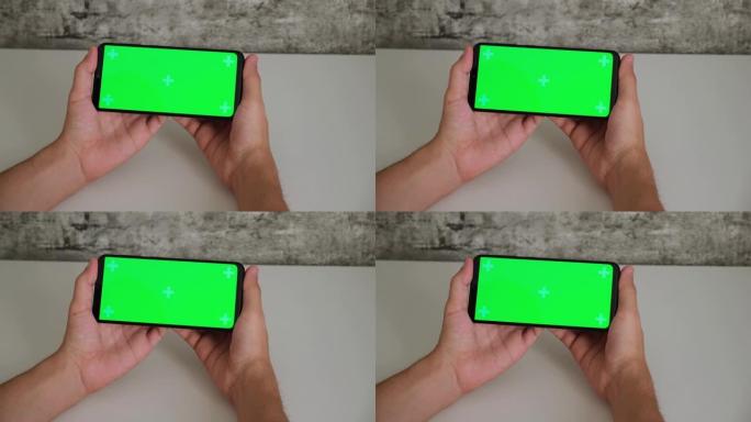 一个坐在白色办公桌前的男人手里拿着手机，屏幕上是绿色的。在智能手机的chromakey屏幕上滑动并点