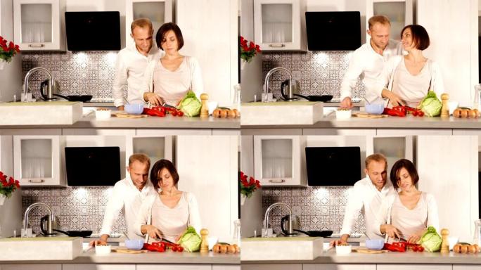夫妇正在厨房准备午餐。女性切蔬菜做沙拉，男人亲切地拥抱她，谈论爱情。一起吃饭准备家庭概念。