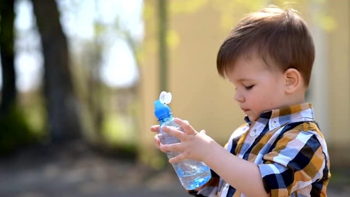 英俊的男孩在外面的晴天从瓶子里喝清水