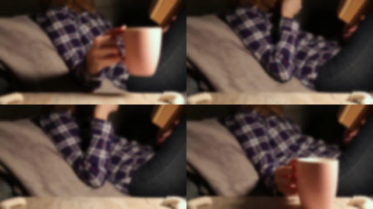 模糊运动。女人喝一杯热咖啡或茶，在沙发上看书。自我隔离时间。检疫时期的娱乐。