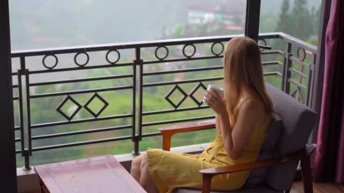 一位年轻的旅行者喜欢坐在一个房间里喝酒，可以看到被云彩覆盖的猫猫谷。南a Pa，越南北部。越南旅游概