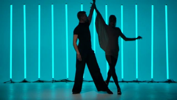 一对舞者表演拉丁美洲舞厅舞伦巴、恰恰恰舞、桑巴舞的元素。一对夫妇的剪影在霓虹灯照亮的黑暗工作室里热情