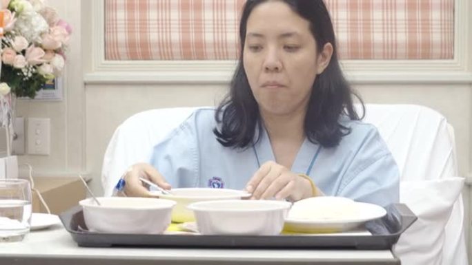 亚洲妇女病人在医院的床上吃饭