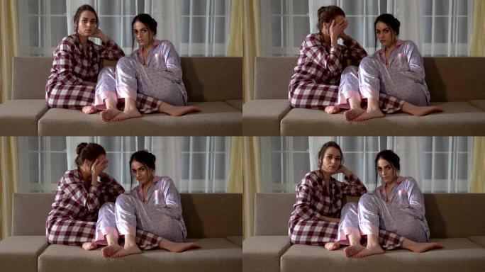 两个穿着睡衣的双胞胎姐妹坐在沙发上，选择在电视上看什么