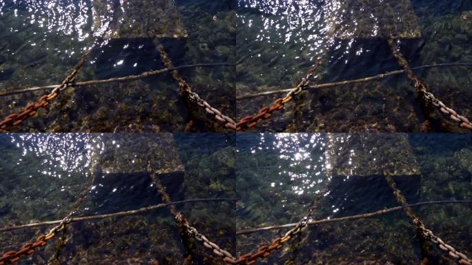 长满藻类的老生锈船链。阳光反射的海水
