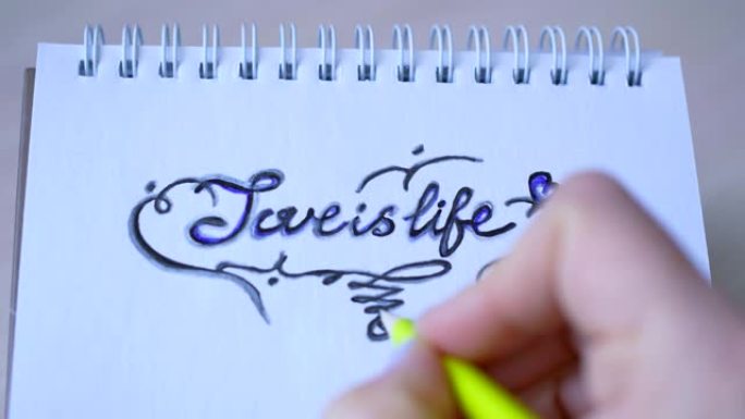 女孩用灰色铅笔在一张记事本上画题词 “爱就是生命”