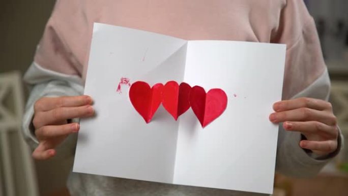 双手展开情人节手工贺卡。我爱你在白纸上涂上红色油漆的标志。