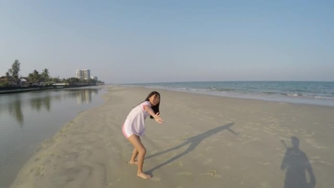 快乐的亚洲女孩穿着白色连衣裙在阳光明媚的日子里在海滩上翻筋斗，生活方式理念。