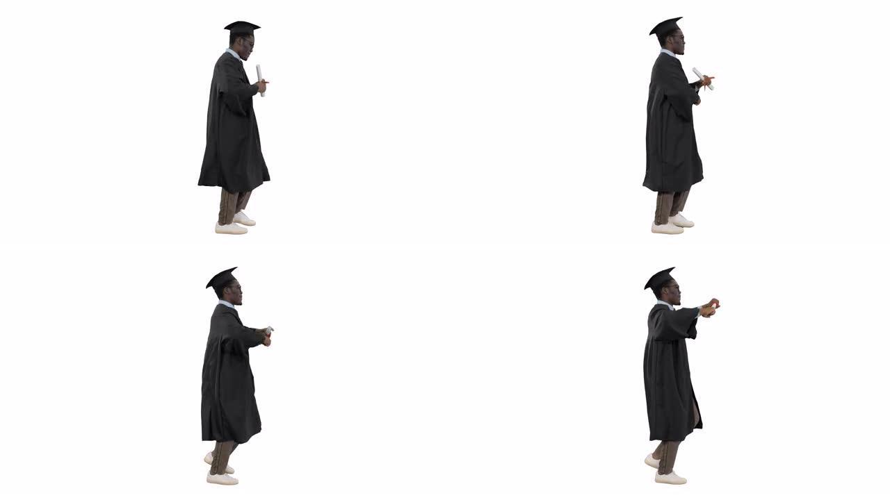 兴奋的非洲裔美国男学生穿着毕业长袍，在白色背景上行走时带着文凭跳舞