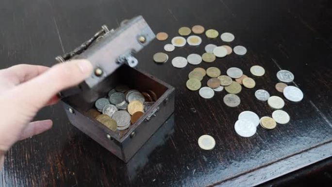 手正在打开带有棕色背景古董硬币的旧棺材，特写。一堆硬币概念