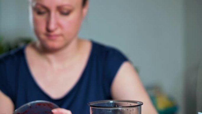 健康饮食的概念。一个女人的特写镜头把一勺水果和浆果泥放在搅拌机里。