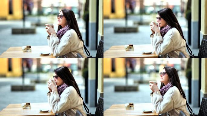 轻松时尚的年轻女子享受休息时间，坐在街边咖啡馆喝热咖啡