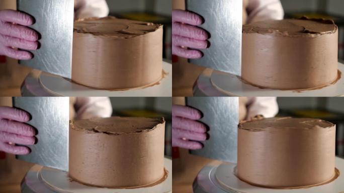 糕点师女人正在烤房的旋转蛋糕架上用金属刮铲在海绵蛋糕上涂抹巧克力奶油。