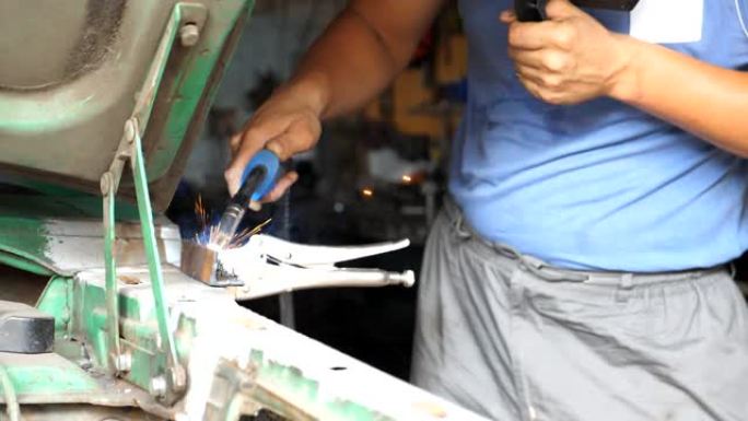 成人汽车制造商的男性手在车库用焊接机焊接旧车的金属零件。修理工或机械工人的手臂在车间使用专业设备进行