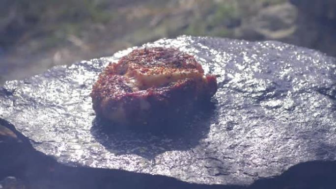 垃圾食品，多汁的肥肥猪肉菲力在篝火上的热石头上油炸，在大自然的营地冒烟