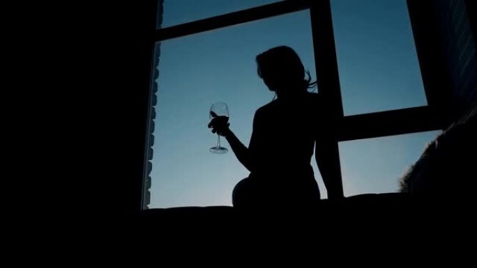 女人剪影在晚上在窗台上的玻璃杯中摇晃葡萄酒