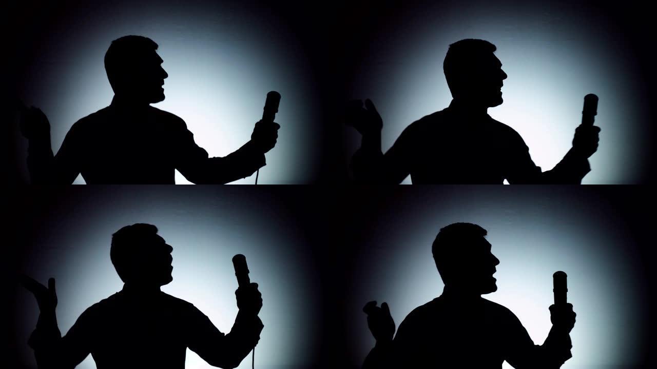 一个男人在浅色背景上的影子。这个人正在用麦克风唱歌。情感，歌曲。