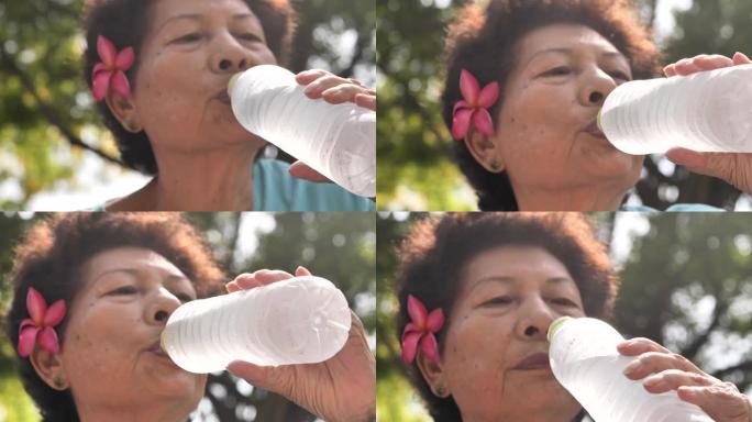 亚洲高级女性从户外的瓶子里喝水，慢动作。