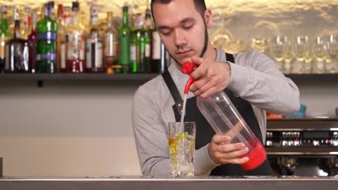 调酒师将苏打虹吸管中的苏打水倒入装满冰块，酸橙和柠檬片的玻璃杯中。