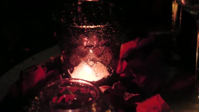 一个玫瑰花瓣周围有蜡烛的杯子