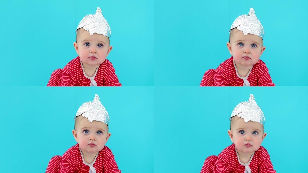 戴着箔纸帽子的婴儿坐在蓝色背景上
