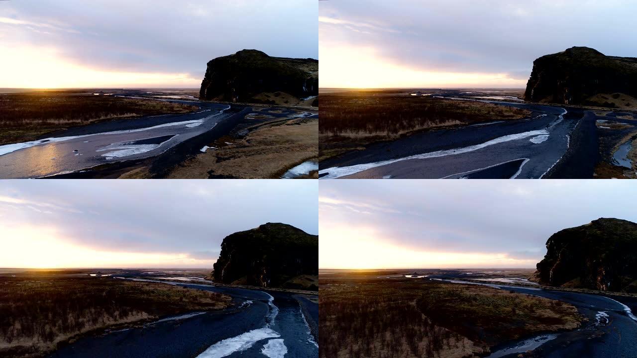 冰岛河流的鸟瞰图。来自瀑布的河流在夕阳下被田野包围。我们可以在背景中看到一座小山。