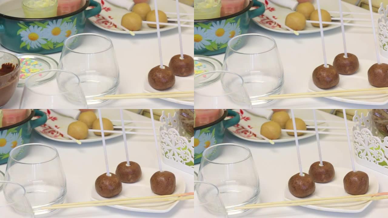 用粘着筷子制作流行蛋糕的饼干球躺在盘子上。桌子旁边是糖衣玻璃杯。