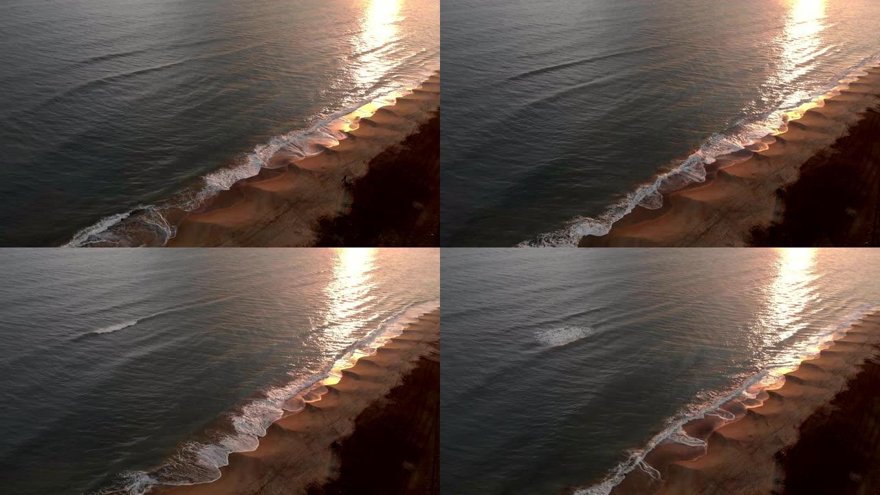 鸟瞰图海上金色的日落，海浪在岸边撞击，美丽的倒影在水面上，远处，一个单独的渔夫，执行冲浪铸造纪律