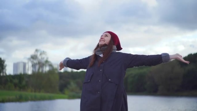 穿着暖和衣服的女人站在河岸上，欢欣鼓舞地张开双臂