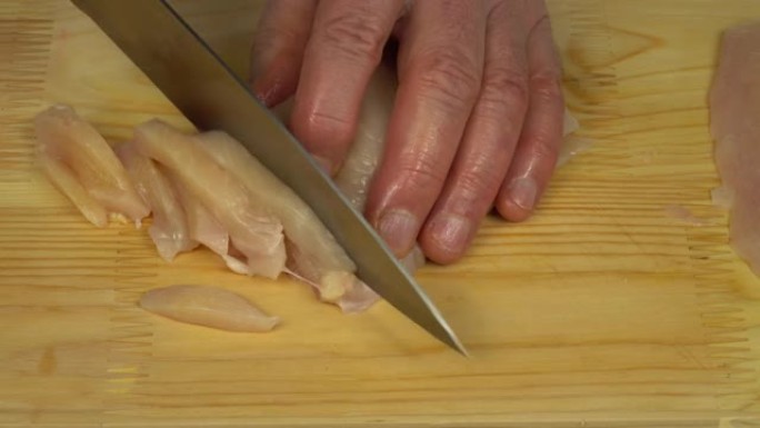 一名男子用锋利的刀在砧板上切成细条的鸡肉白肉，煮鸡肉stroganoff