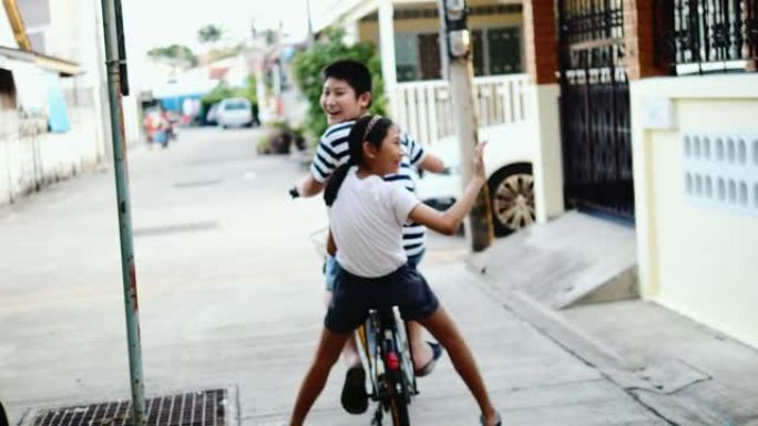 快乐的亚洲男孩和他的妹妹一起骑自行车从房子到公园巷，生活方式理念。