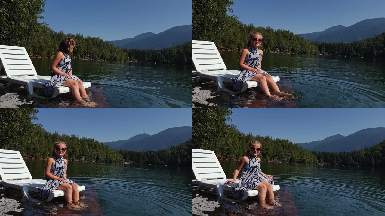 小女孩戴着太阳镜和波西米亚丝绸披肩躺在日光浴床上。儿童在洪水木水下码头上休息。湖面上铺满了水。