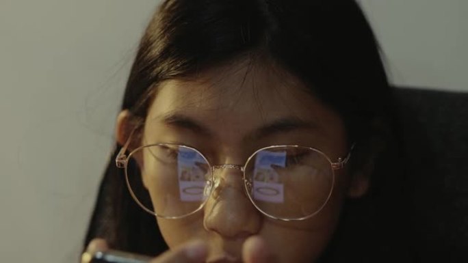 亚洲女孩戴着眼镜使用智能手机在晚上在家，生活方式概念。
