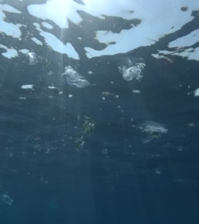 垂直视频: 巨大的塑料和其他碎片在太阳光线下缓慢地漂移在蓝色海洋的表面下。塑料垃圾环境污染问题。海洋