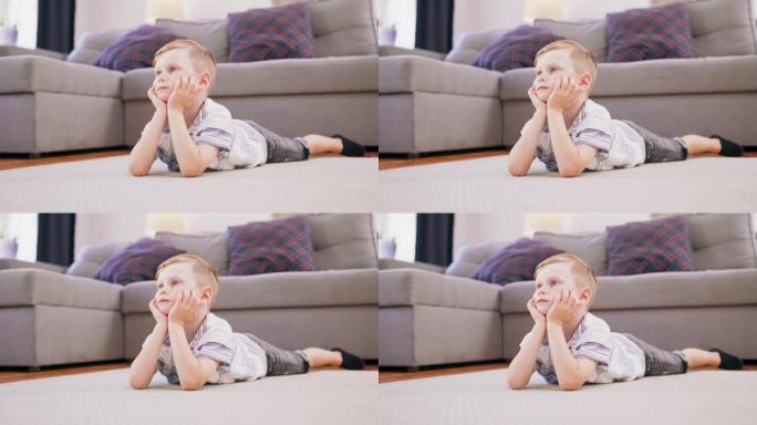 可爱的金发小男孩躺在地板上盯着电视上他最喜欢的动画片