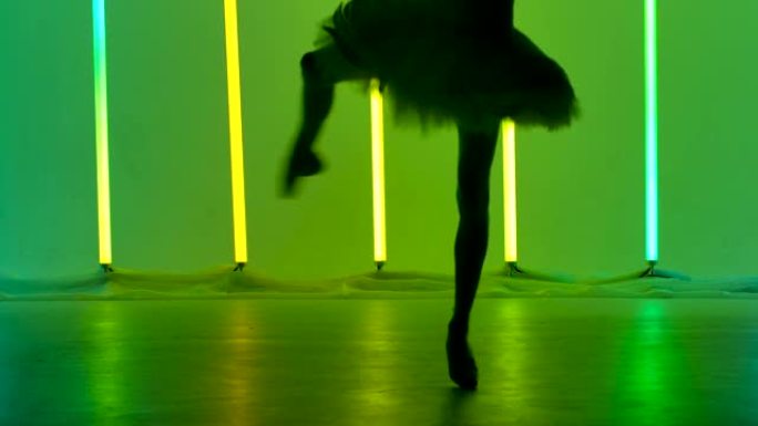 优雅的芭蕾舞演员正在跳舞白天鹅的一部分，表演旋转木马。在黑暗的工作室中，苗条的身材在明亮的霓虹灯的背