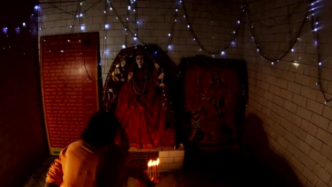 穿着橙色衣服的印度教女神杜尔加·和尚雕像附近的傍晚aarti敲响钟声，并用燃烧的灯具重复动作
