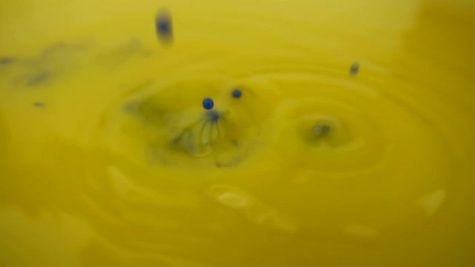 黄色油漆背景的微距摄影。蓝色油漆在慢动作中滴在黄色油漆上。
