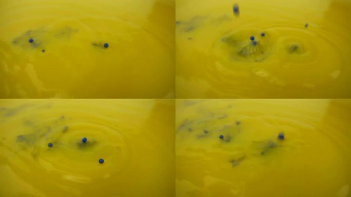 黄色油漆背景的微距摄影。蓝色油漆在慢动作中滴在黄色油漆上。